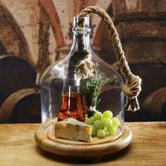 a glass bottle with wine, cheese and grapes on a wooden plate next to some barrels