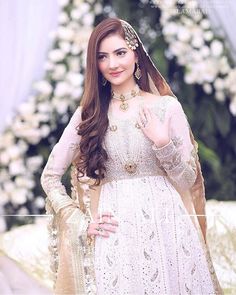 a woman in a white and gold bridal gown posing for the camera with her hand on her hip