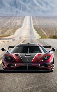 a red and black sports car driving down the road with mountains in the back ground