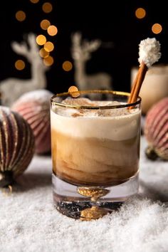 a glass filled with liquid sitting on top of snow covered ground next to christmas ornaments