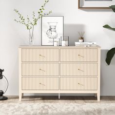 a white dresser sitting next to a plant in a room with pictures on the wall