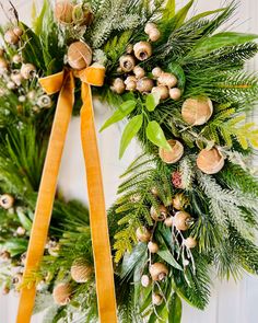 two wreaths hanging on the wall with pine cones and greenery tied around them