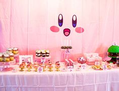 a table topped with lots of desserts and cupcakes next to a pink wall