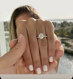 a woman holding up her engagement ring in front of the camera with water behind her