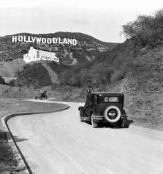 an old black and white photo of a car driving down the road with hollywood land in the background