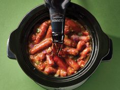 a crock pot filled with hot dogs and sauce being poured into the slow cooker