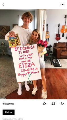 a man and woman holding a sign in front of a room with guitars on the wall