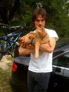 a man holding two cats in front of his car