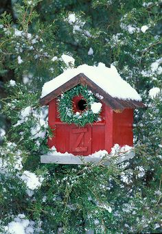 a red birdhouse with a wreath on it's roof