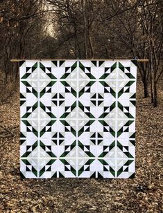 a black and white quilt hanging on a clothesline in the woods with leaves around it