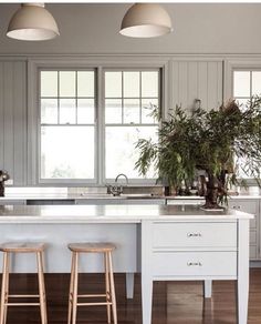 a kitchen with two stools next to an island in front of the sink and windows