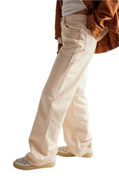 A person wearing beige wide-leg jeans, a white top, and a brown jacket. The jeans have a relaxed fit, and the person is also wearing beige sneakers with light brown soles. Beige Cargo Jeans With Patch Pockets For Streetwear, Oversized Straight Leg Jeans For Workwear, Beige Cargo Jeans For Fall, Fall Beige Cargo Jeans, Beige Baggy Cargo Jeans For Streetwear, Cream Cotton Jeans Relaxed Fit, Cream Cotton Jeans With Relaxed Fit, Fall Beige Cargo Jeans With Side Pockets, Cream Cotton Relaxed Fit Jeans