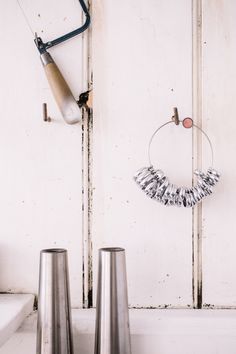 two silver vases sitting next to each other on a white counter with a metal object hanging from it's side