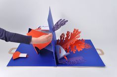 a person cutting out paper with scissors on top of an orange and blue piece of art