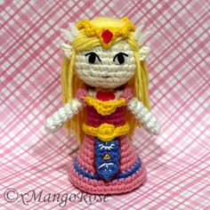 a crocheted doll with blonde hair and blue eyes, wearing a pink dress