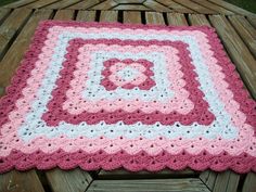 a pink and white crocheted blanket sitting on top of a wooden bench