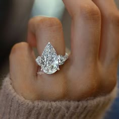 a woman's hand holding an engagement ring with two pear shaped diamonds on it