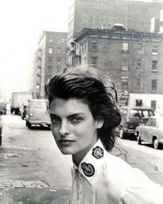 black and white photograph of a woman standing on the side of a road with buildings in the background