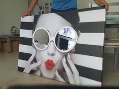 a woman holding up a large poster with sunglasses on it's face and red lips