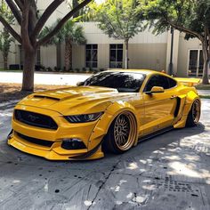 a yellow ford mustang parked in front of a building with trees and bushes around it