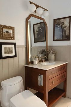 a white toilet sitting next to a wooden sink vanity in a bathroom under a mirror