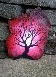 a rock with a tree painted on it sitting in front of a stone wall,