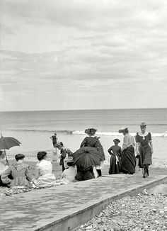 black and white photograph of people sitting on the beach with umbrellas over their heads