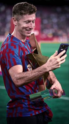 a man holding a trophy and looking at his cell phone while standing on a soccer field