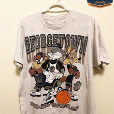 Vintage Ncaa Georgetown Hoyas Looney Tunes T-Shirt, Georgetown Hoyas Shirt, Georgetown University Shirt, Unisex Shirt, Vintage Shirt Our Classic T-Shirt Serves As The Perfect Short-Sleeved Shirt For Your Unique, Funny, Or Personalized Designs. Brand: Gildan Heavy Weight Fabric Classic Unisex Makes This An Easy Fit Size Up If You Want Something Roomier Our Shirts Materials: 100% Cotton ** Note: - Double Check Your Address Before Ordering. - If You Want To Return The Goods, You Are The One To Pay Throwback Cotton Fan Merchandise Tops, Throwback Cotton Tops For Fan Merchandise, Character Print Crew Neck Top For College, Sporty Tops With Character Print For Fans, Gray Graphic Tee With Character Print, Gray Graphic Print Fan Apparel Top, Casual Gray Tops With Character Print, Throwback Short Sleeve Top For College, Throwback Short Sleeve Top