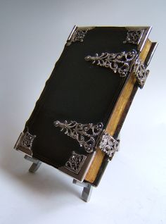 an open book with ornate silver decorations on the front and sides, sitting on a white surface