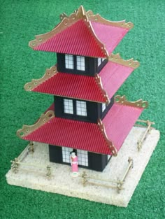 a doll house with red roof sitting on top of green grass