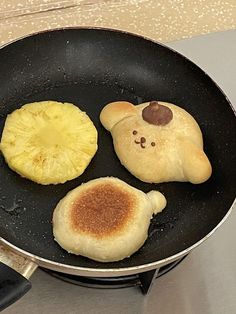 three pancakes are being cooked in a frying pan on the stove top, with one pineapple and two bananas