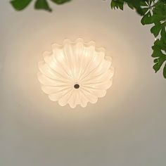 a white ceiling light with green leaves hanging from it's center point on a gray wall