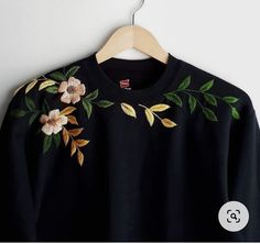 a black sweater with flowers and leaves embroidered on the front, hanging from a hanger