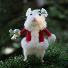 a needle - felt mouse ornament is hanging on a christmas tree branch with a bell