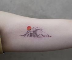 a small wave tattoo on the arm with an orange sun in the distance behind it