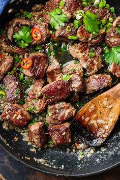 meat and vegetables cooking in a skillet with a wooden spoon on the side, ready to be eaten