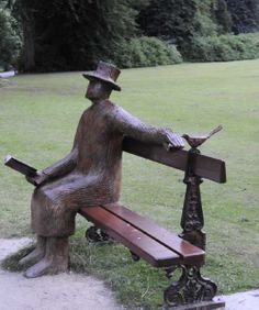 a statue of a man sitting on top of a wooden bench next to a park