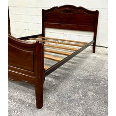 a wooden bed frame with slatted headboard and foot board on concrete ground