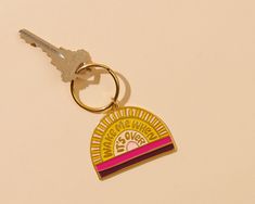 a keychain with a pink and yellow design on the front is sitting next to a pair of keys