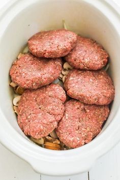 several hamburger patties in a white crockpot with nuts and seasoning on the side