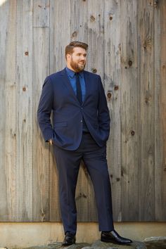 a man in a suit and tie leaning against a wooden wall with his hands in his pockets