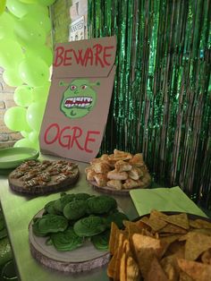 a table topped with lots of food next to green foily balloons and streamers