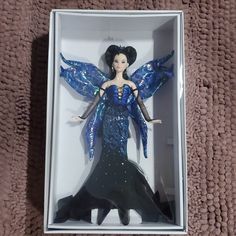 a barbie doll in a box on a brown carpeted floor with her wings spread out