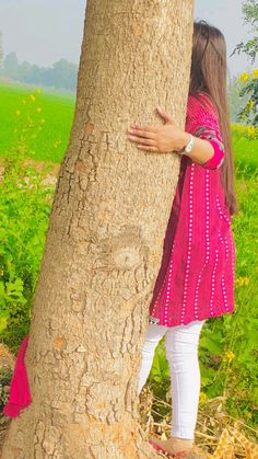 a woman hugging a tree in the middle of a field