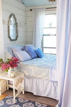 a bed with blue and white decor in a bedroom next to a table with flowers on it