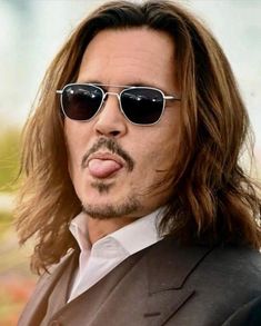 a man with long hair and sunglasses making a funny face while wearing a black suit