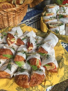 many sandwiches are wrapped in white paper on a yellow tablecloth next to other food items