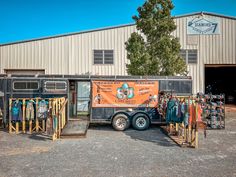 Old horse trailer turned into mobile boutique setup in front of indoor horse riding arena with t-shirt and hanging racks set up in front of trailer Horse Trailer Boutique, Boutique Trailer Mobile Shop, Western Boutique Display, Retail Trailer, Trailer Boutique, Plus Size Western Fashion, Graphic Tees Western, Vendor Setup