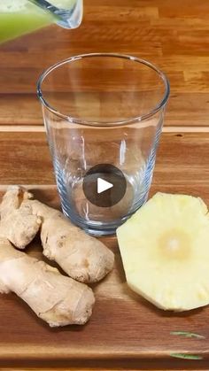 a wooden cutting board topped with sliced up ginger next to a glass of green smoothie